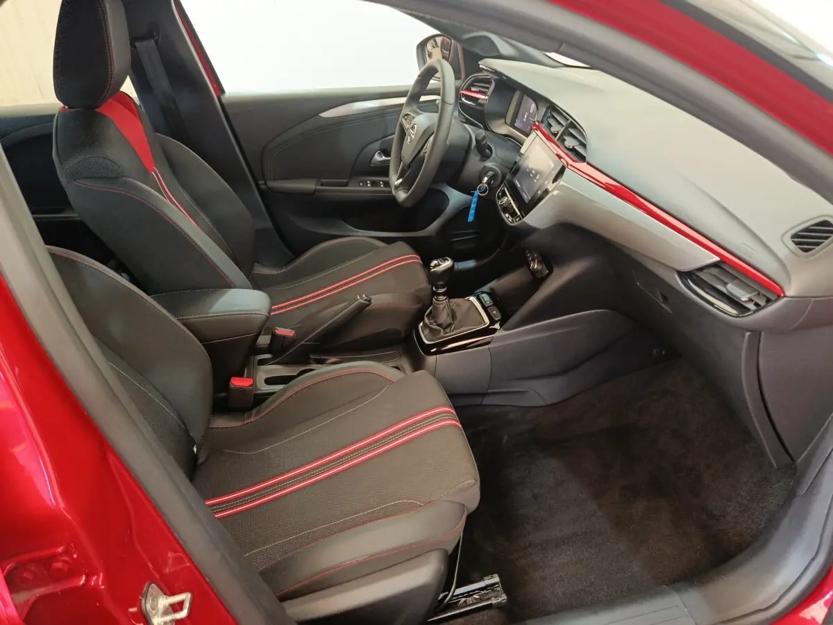 Intérieur avant droit de l’Opel Corsa rouge 2023, sièges noirs avec surpiqûres rouges et tableau de bord moderne.