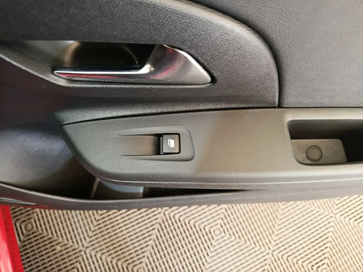 Détail de la poignée intérieure et commande de vitre sur la porte côté gauche d’une Opel Corsa rouge.