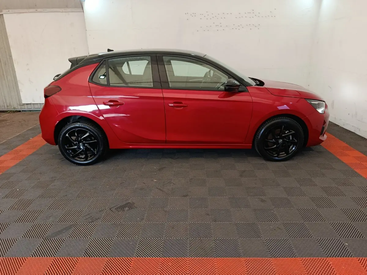 Vue de profil côté gauche d'une Opel Corsa rouge 2023 avec toit noir et jantes noires brillantes.