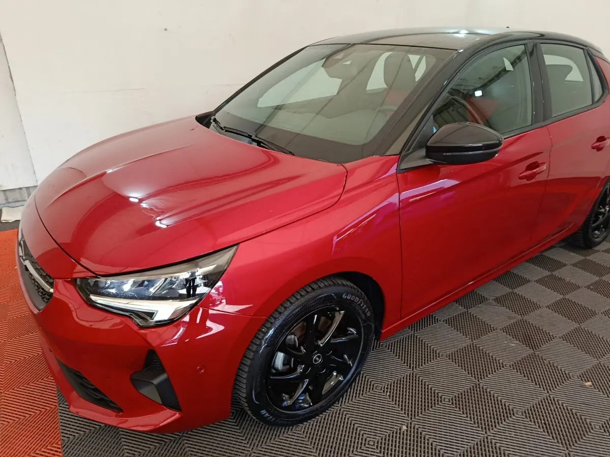 Vue 3/4 avant droite d’une Opel Corsa rouge 2023 avec toit noir et jantes noires brillantes.