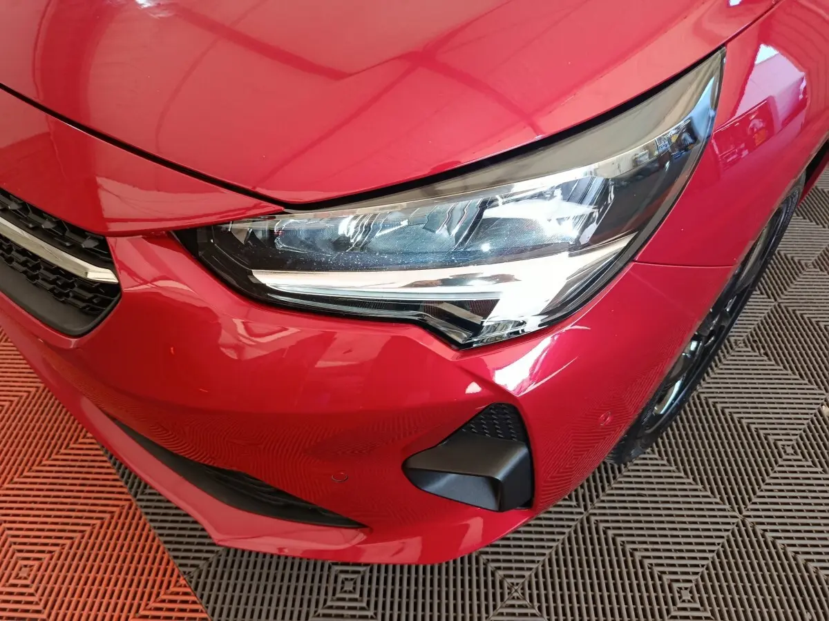 Gros plan sur l'avant droit rouge vif de l'Opel Corsa 2023, mettant en valeur le phare LED et la calandre.