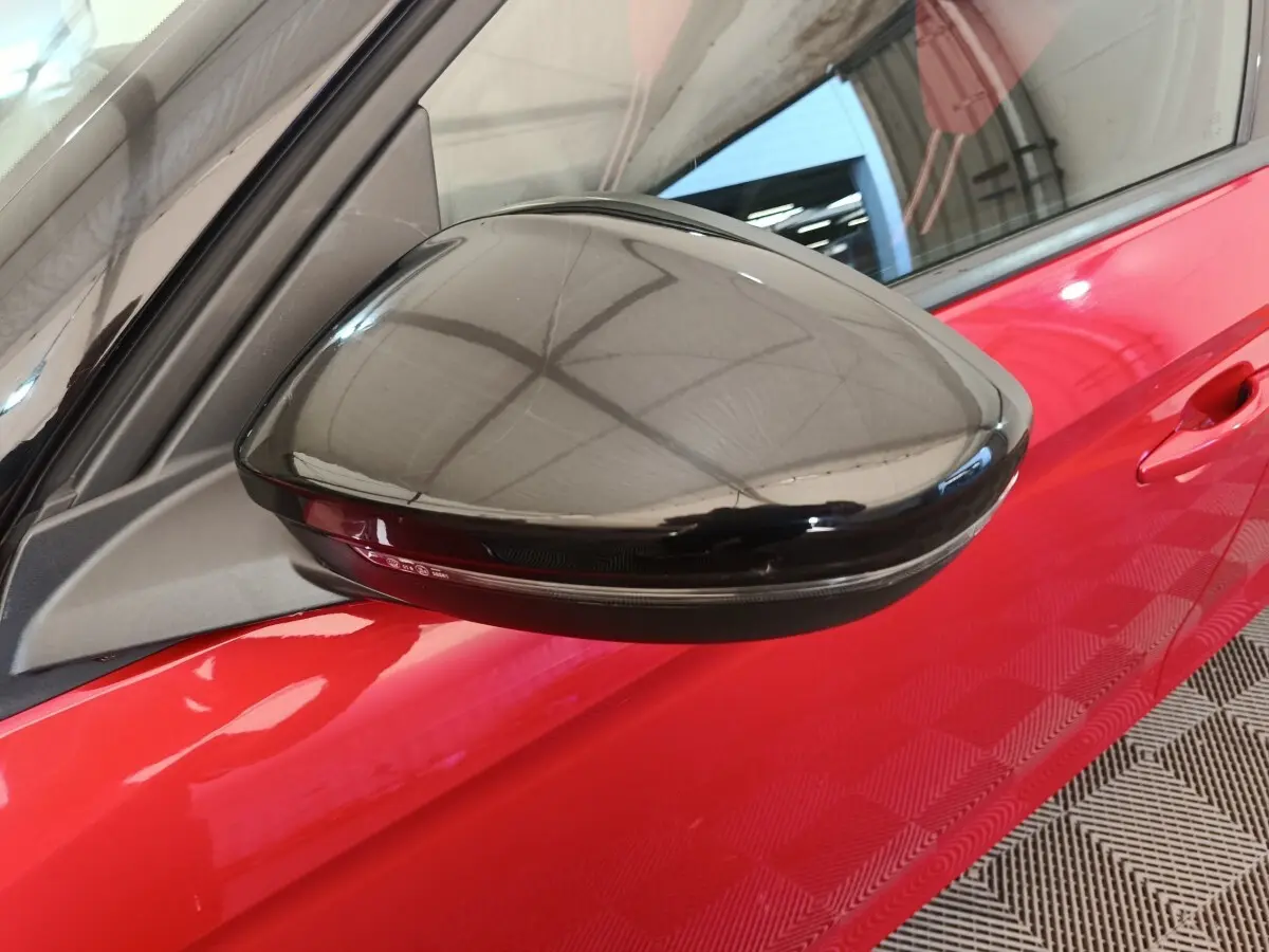 Gros plan sur le rétroviseur noir côté gauche de l’Opel Corsa rouge 2023, avec porte visible en arrière-plan.
