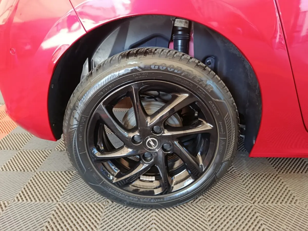 Gros plan sur la roue avant gauche noire brillante d’une Opel Corsa rouge 2023, avec logo Opel au centre.