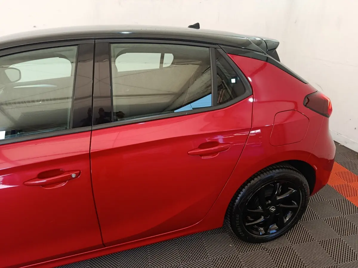 Vue latérale droite d'une Opel Corsa rouge 2023 avec toit noir et jantes noires brillantes.