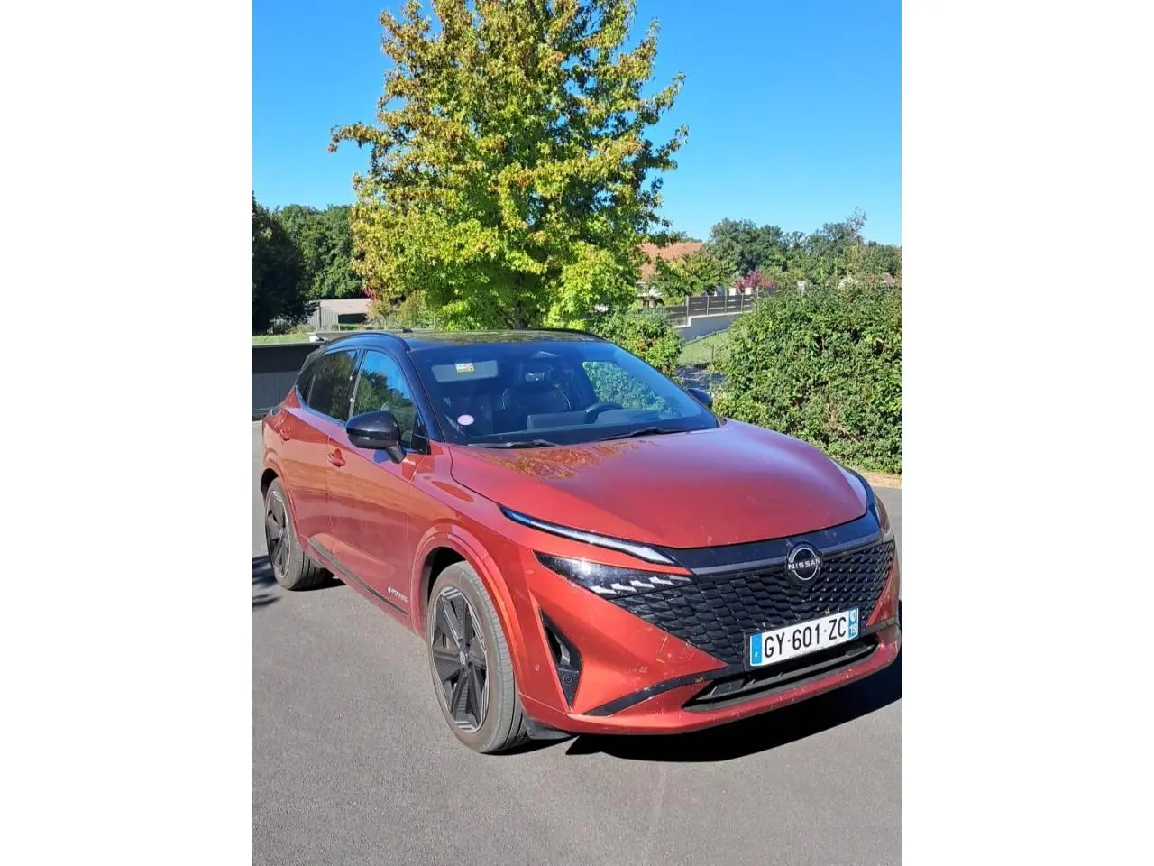 Nissan Qashqai 2024 rouge foncé en 3/4 avant droit, avec calandre noire et jantes noires distinctives.