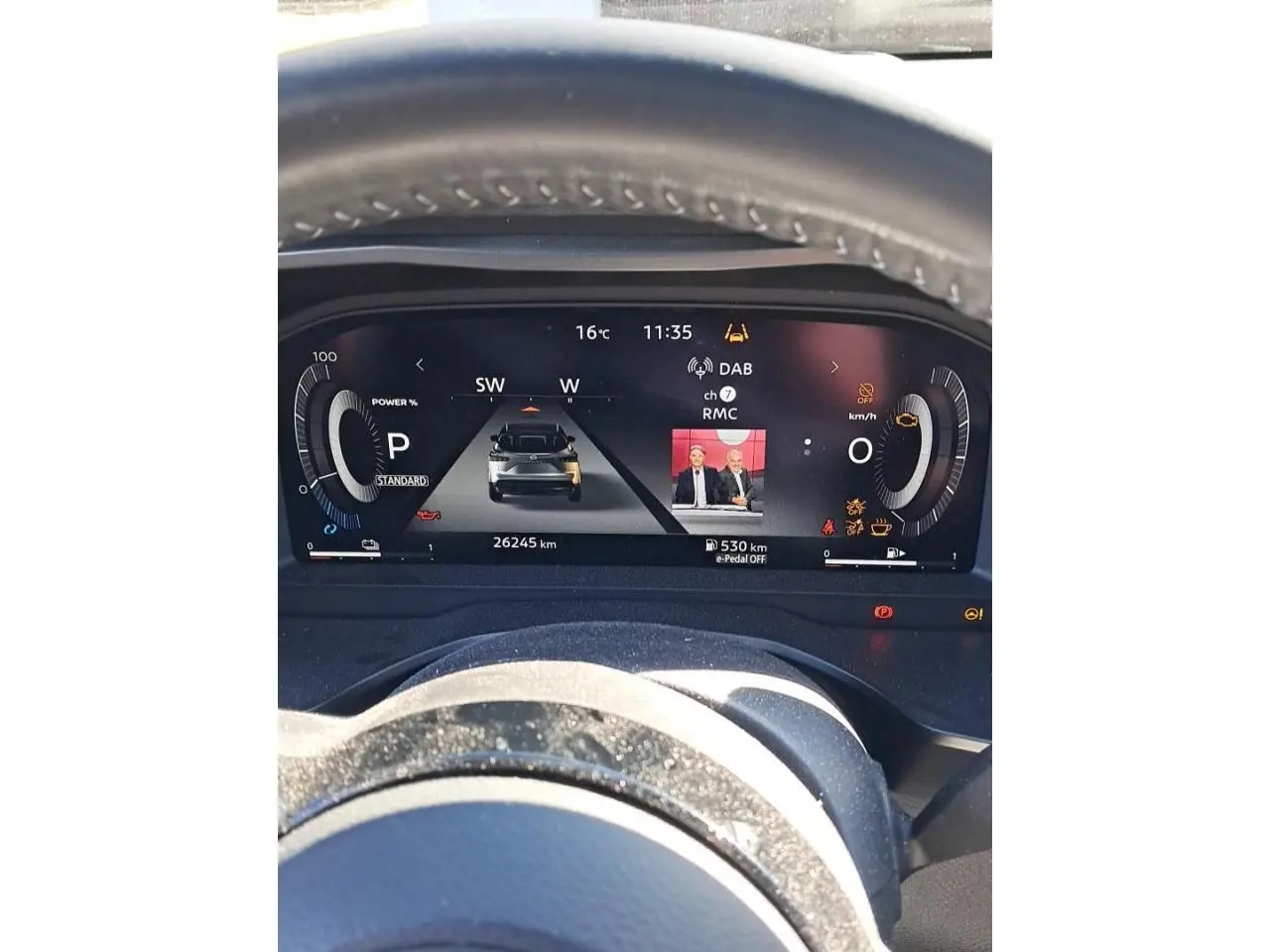Vue rapprochée du tableau de bord numérique du Nissan Qashqai 2024 rouge foncé, affichant les informations de conduite et médias.