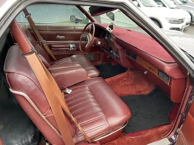 Vue intérieure côté conducteur du Ford Aerostar Ranchero Squire 1979 en bordeaux, avec tableau de bord et sièges en cuir assortis.