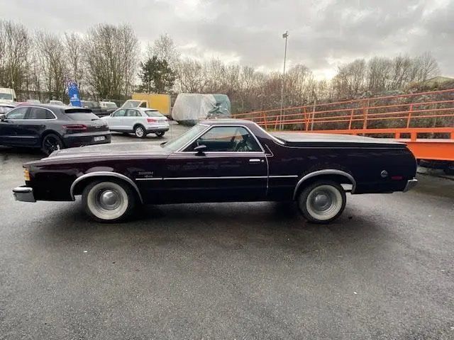 Profil droit d'une Ford Aerostar Ranchero Squire 5.7L bordeaux métal de 1979 avec capot arrière fermé sur parking.