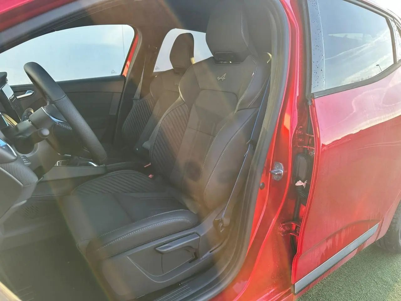 Vue intérieure côté conducteur d'une Renault Clio V rouge flamme avec sièges Esprit Alpine noirs brodés.