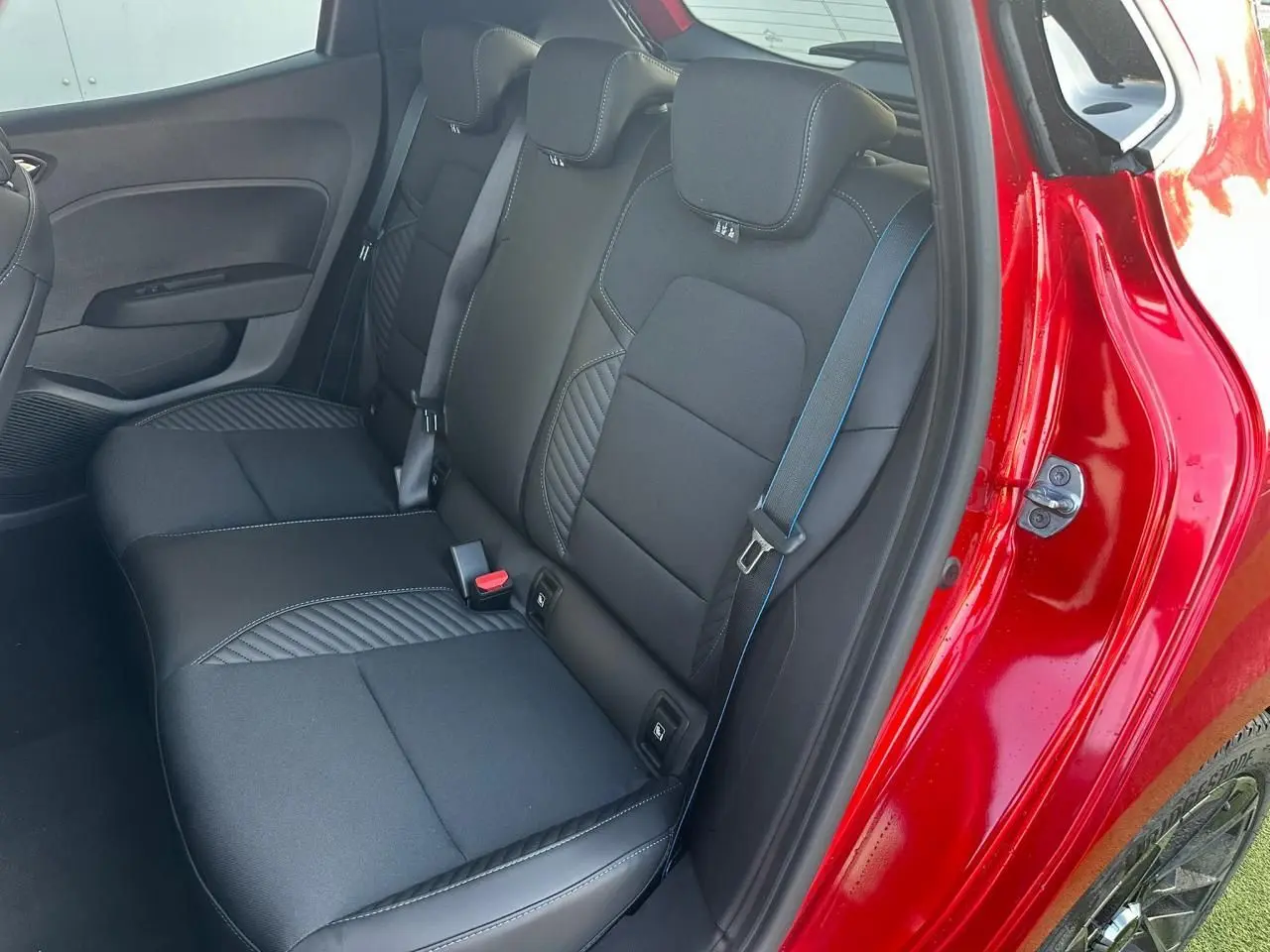 Vue côté droit sur la banquette arrière noire avec surpiqûres bleues d'une Renault Clio V rouge flamme.