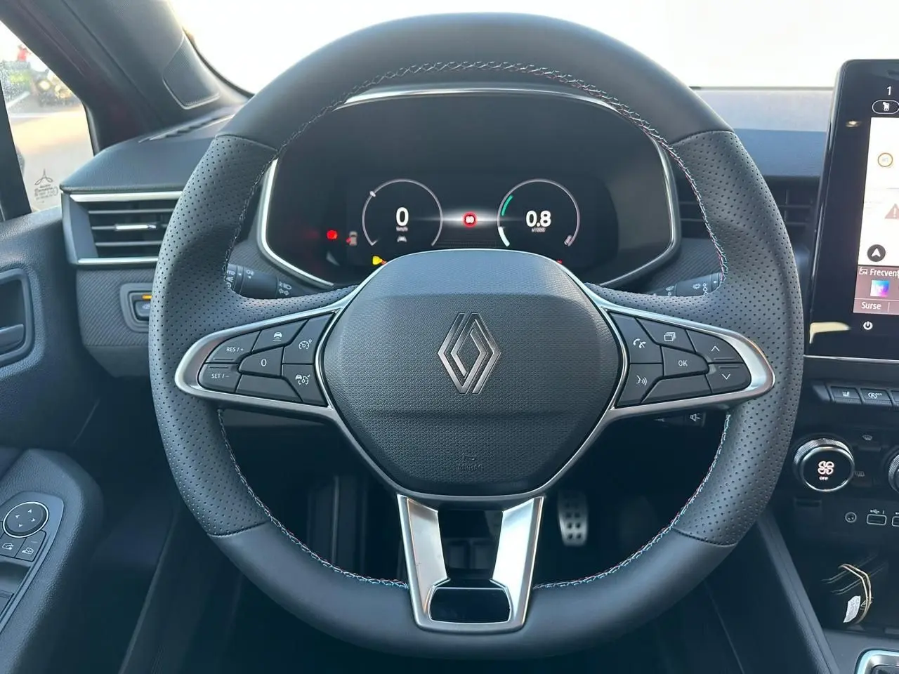 Volant multifonction noir avec surpiqûres tricolores et logo Renault, tableau de bord numérique d'une Renault Clio V rouge flamme métal.