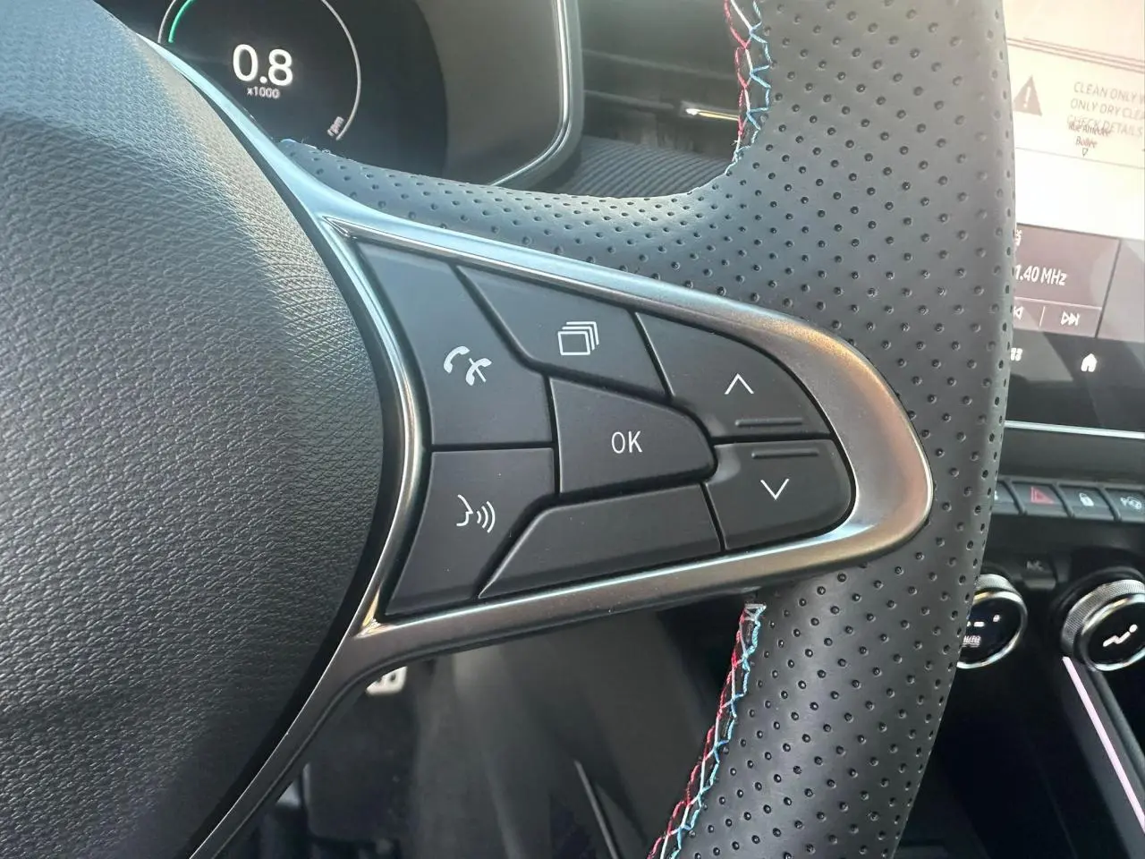 Gros plan sur les commandes du volant perforé avec surpiqûres tricolores de la Renault Clio V Esprit Alpine.