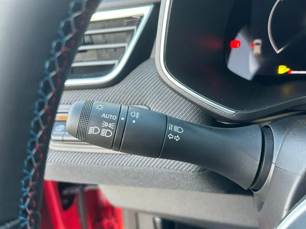 Gros plan sur la commande des feux et clignotants à gauche du volant d'une Renault Clio V rouge flamme metal.