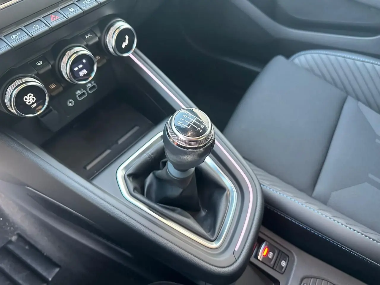 Gros plan sur levier de vitesse manuel et console centrale noire avec surpiqûres bleues dans Renault Clio V Esprit Alpine.