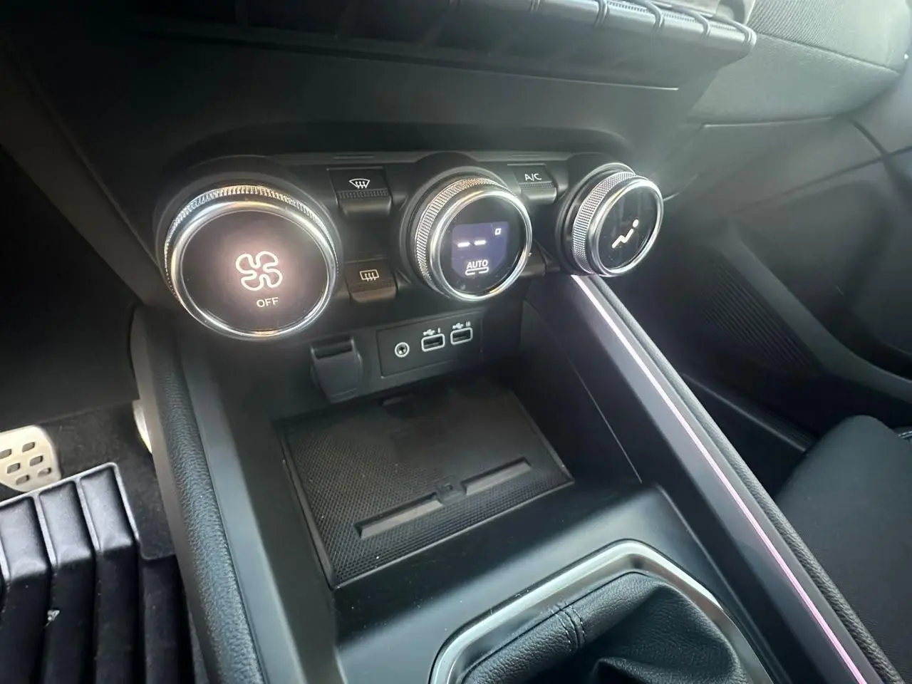 Gros plan sur la console centrale de la Renault Clio V rouge flamme, montrant les commandes de climatisation et ports USB.