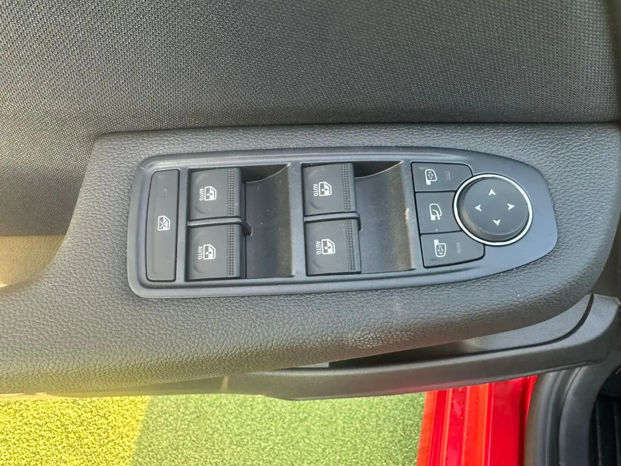Commande des vitres électriques et réglage des rétroviseurs sur la porte côté gauche d'une Renault Clio rouge flamme.