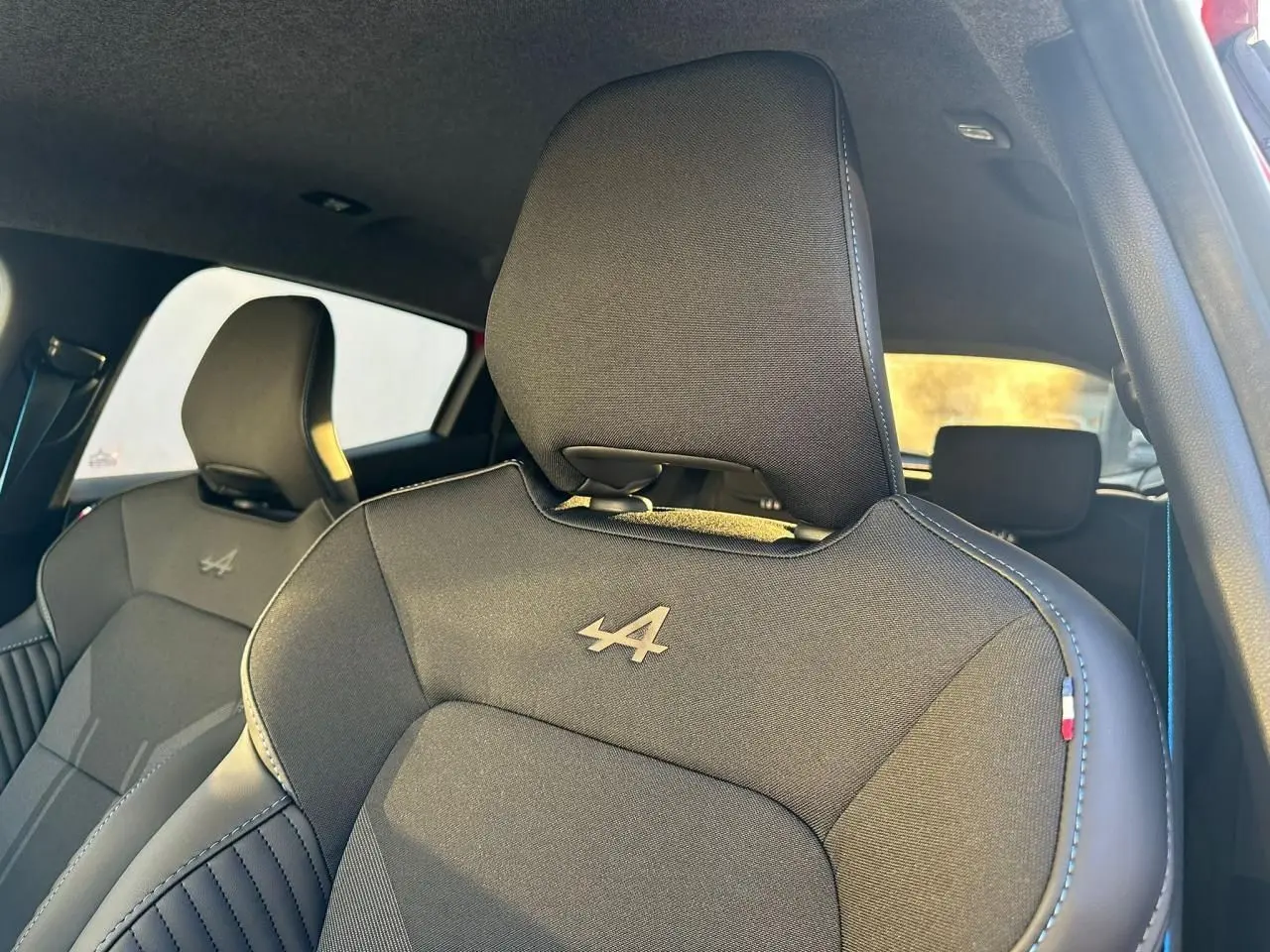 Gros plan sur les sièges avant noirs avec logo Alpine et surpiqûres bleues dans une Renault Clio V rouge flamme.