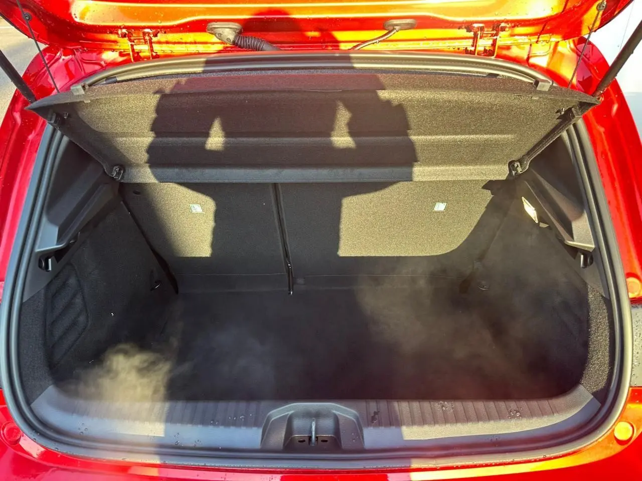 Coffre ouvert vu de dessus d'une Renault Clio rouge flamme métal, montrant l'espace de chargement intérieur.