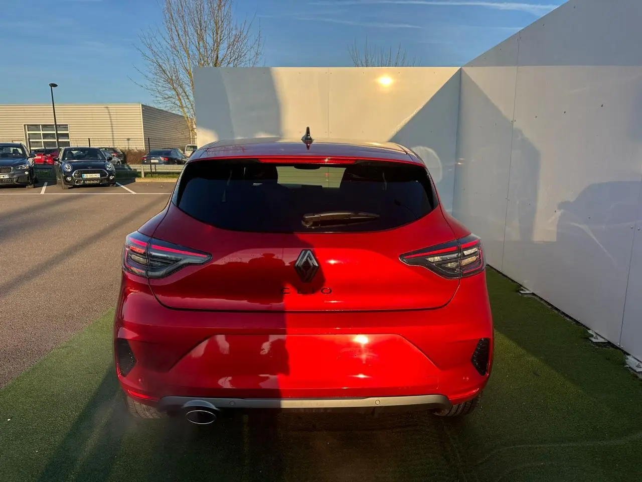 Vue arrière d'une Renault Clio rouge flamme métal avec feux LED en forme de C et antenne requin noire.