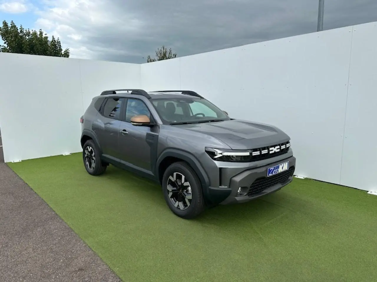 Dacia Duster III gris schiste métal vu en 3/4 avant droit avec barres de toit noires et jantes alliage.