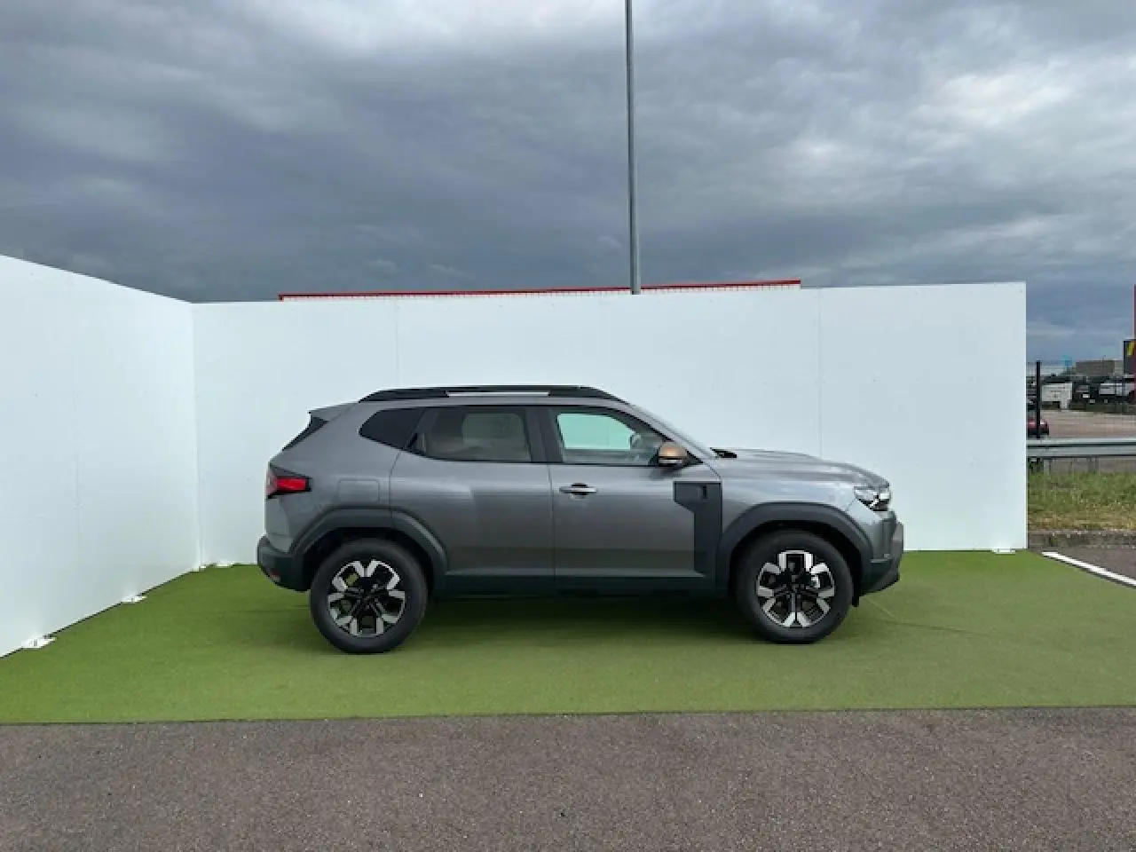 Profil côté gauche du Dacia Duster III gris schiste métal avec jantes alliage et barres de toit noires sur fond extérieur.
