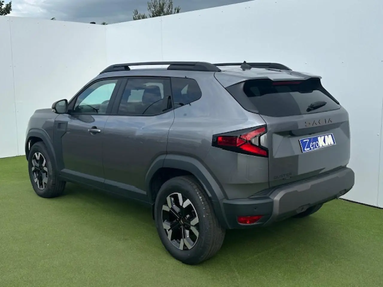 Vue 3/4 arrière droite du Dacia Duster III gris schiste métallisé avec barres de toit noires et jantes alliage 17 pouces.