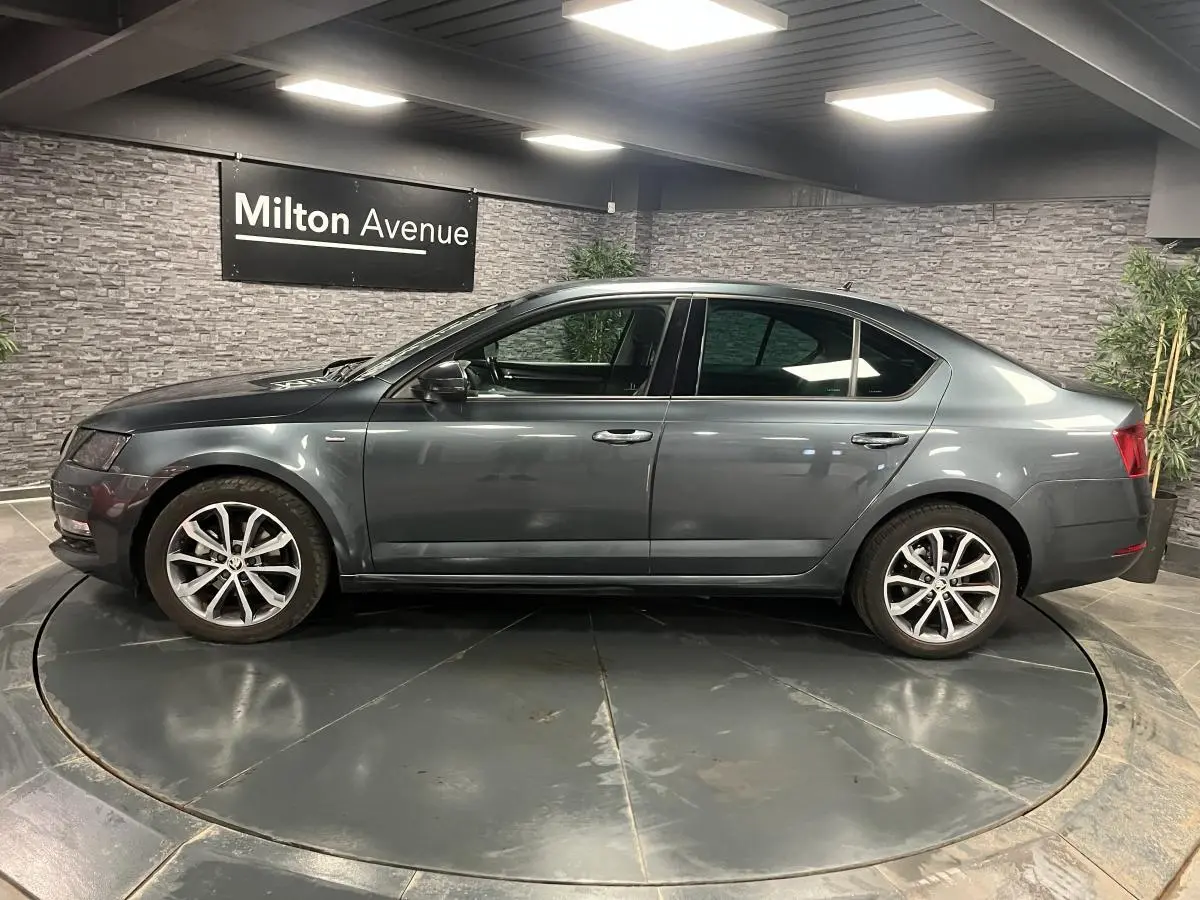 Profil côté gauche d'une Skoda Octavia gris métallisé 2020 en berline, avec jantes alliage 17 pouces, en intérieur showroom.