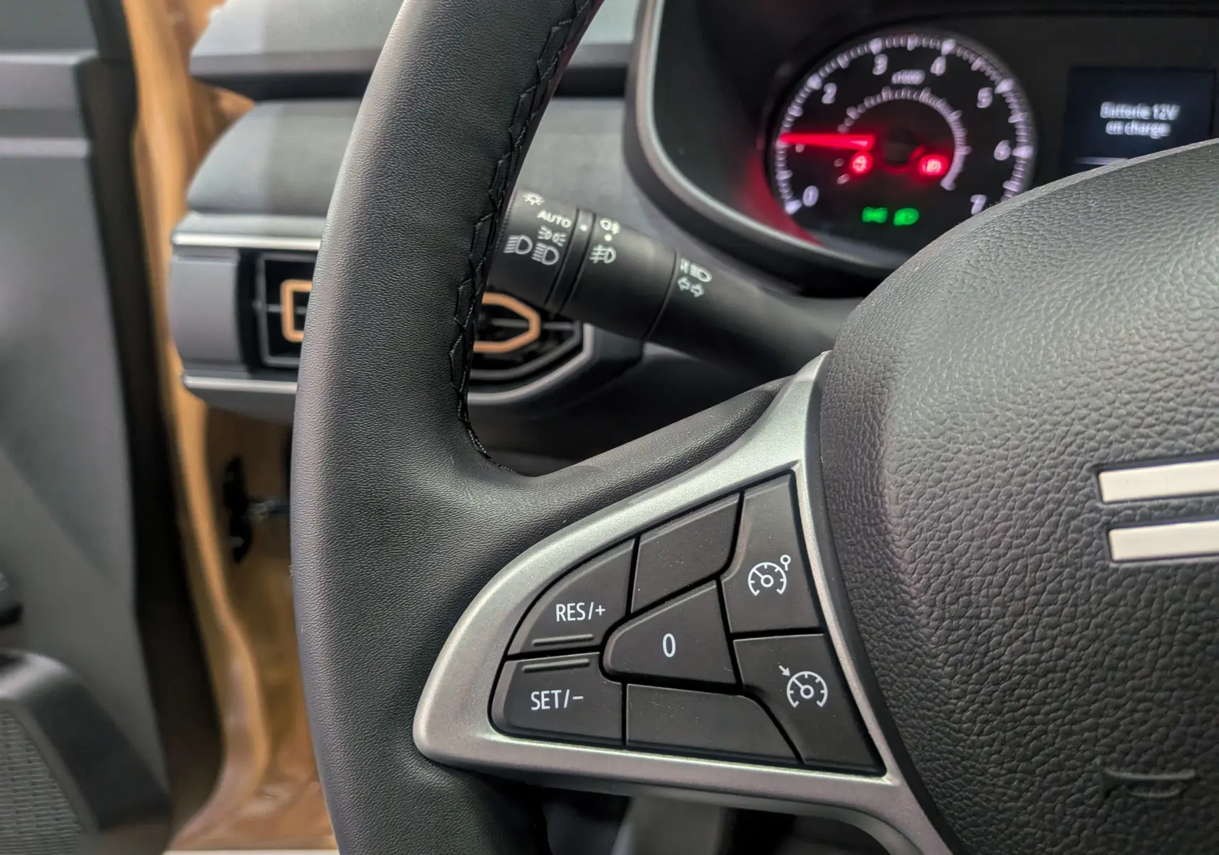 Gros plan sur le volant noir et tableau de bord du Dacia Sandero Stepway beige Safari, avec commandes de régulateur de vitesse.