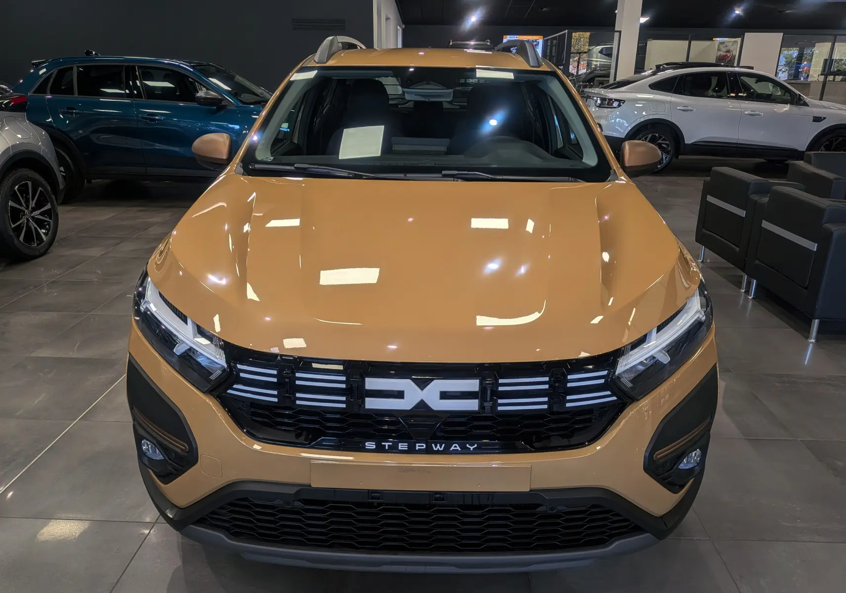 Vue avant d'une Dacia Sandero Stepway beige Safari 2025 en showroom, avec calandre noire et logo distinctif.