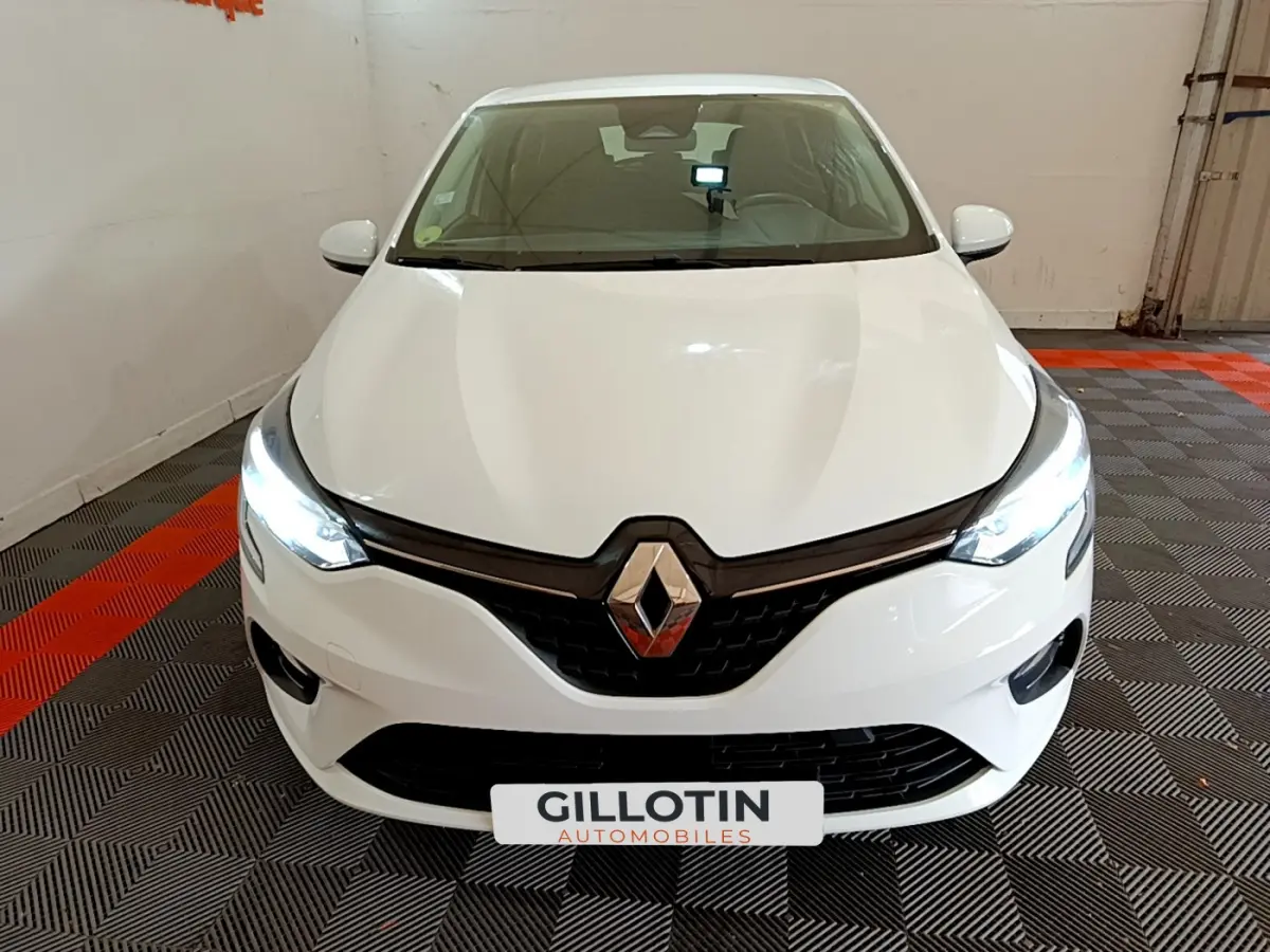 Vue frontale d'une Renault Clio blanche 2020 avec phares LED allumés dans un garage au sol carrelé noir et rouge.