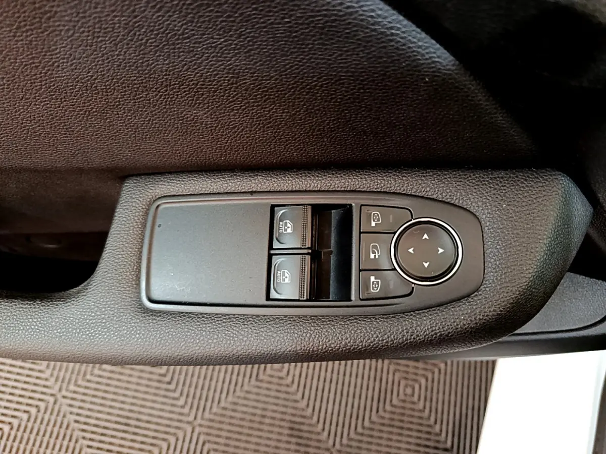 Gros plan sur les commandes de lève-vitres et réglages des rétroviseurs côté conducteur d'une Renault Clio blanche 2020