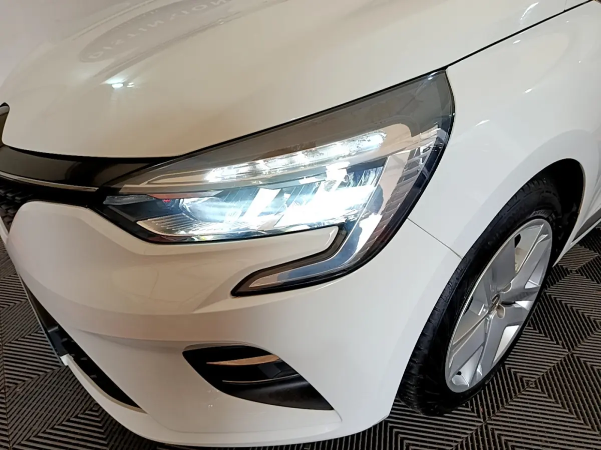 Gros plan sur l'avant droit blanc d'une Renault Clio 2020, mettant en valeur le phare LED allumé et la jante alu.