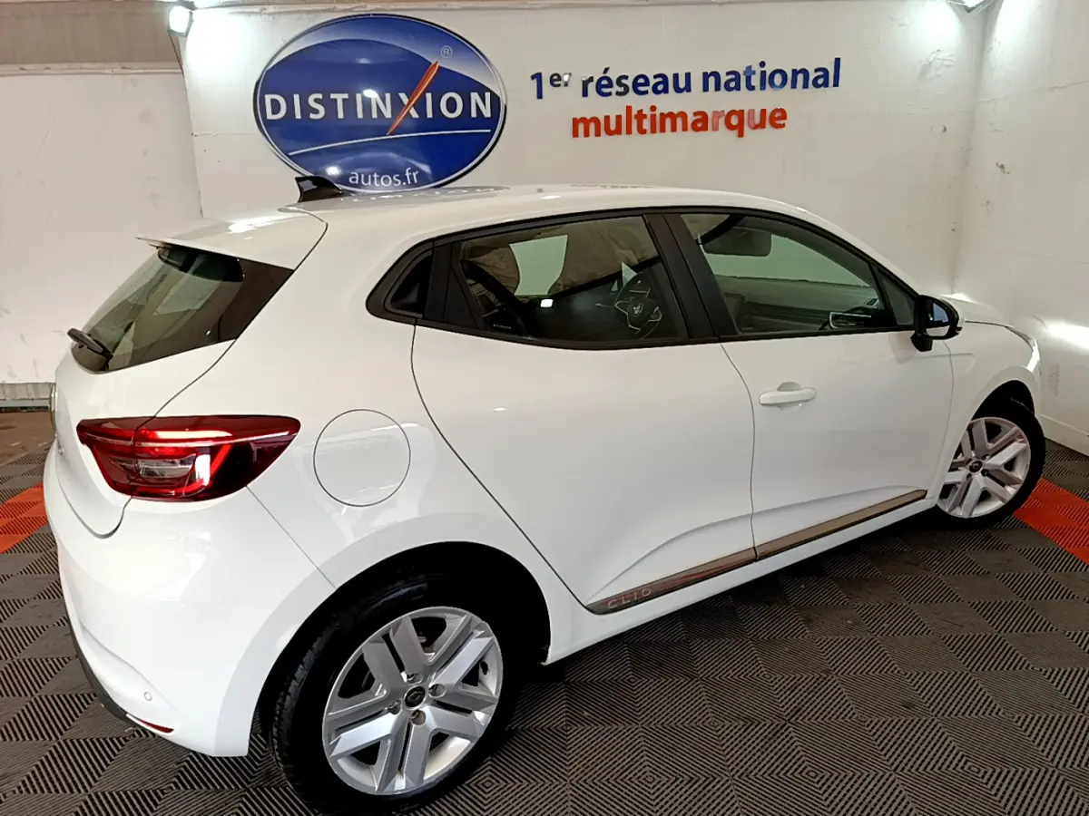 Vue de profil côté droit d'une Renault Clio Business Blue dCi 85 blanche en intérieur avec feux arrière allumés.