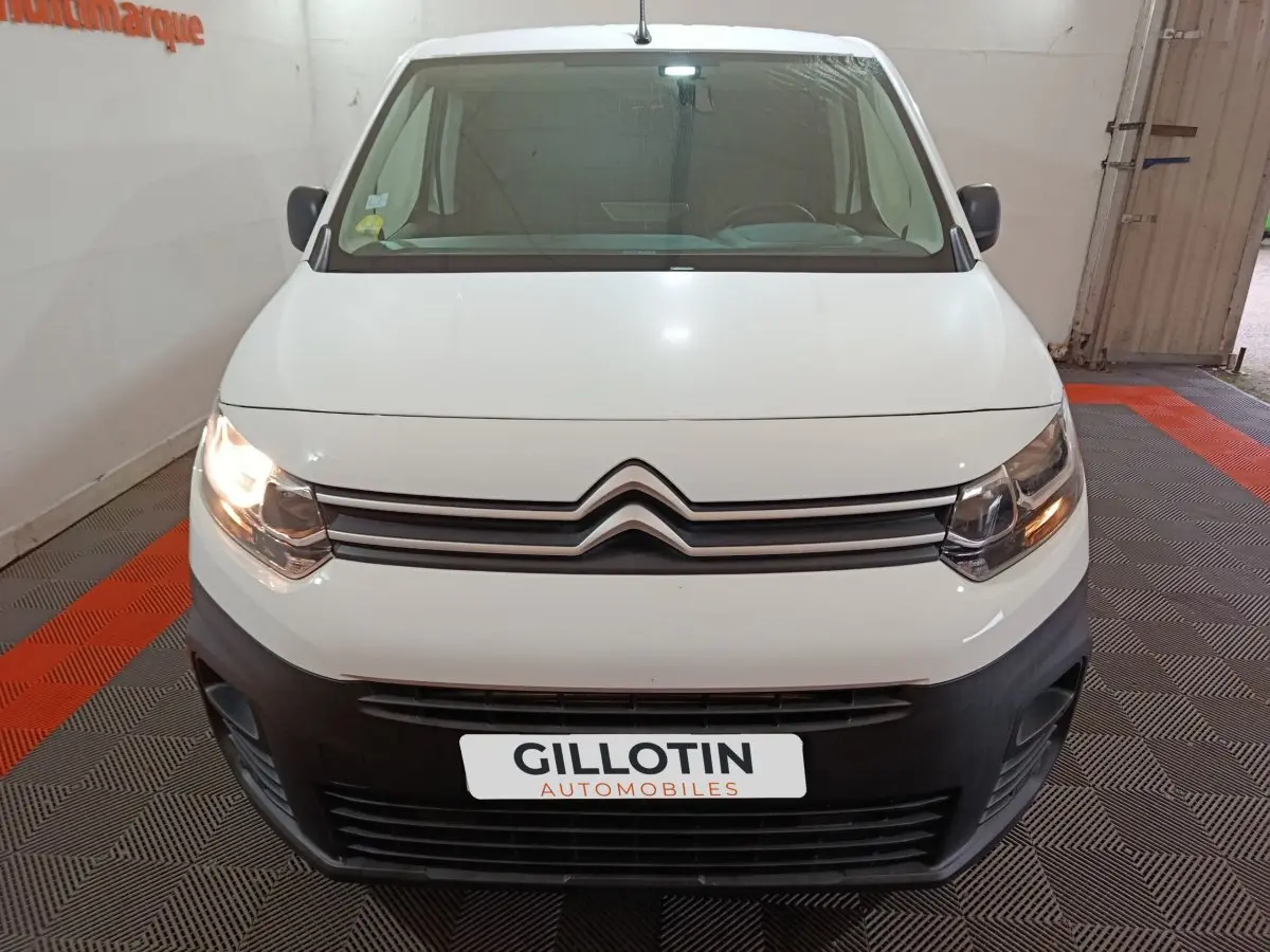 Vue frontale d'un Citroën Berlingo blanc 2021 avec phares allumés et pare-chocs noir dans un garage.