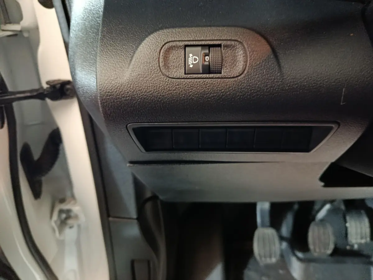 Détail du tableau de bord noir côté gauche avec réglage manuel des phares sur Citroën Berlingo blanc 2021.