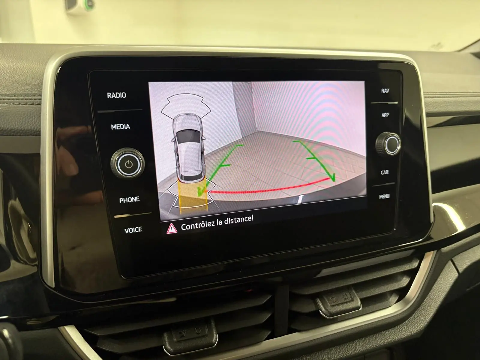 Écran central affichant la caméra de recul avec vue aérienne du Volkswagen T-Roc blanc pur en stationnement.