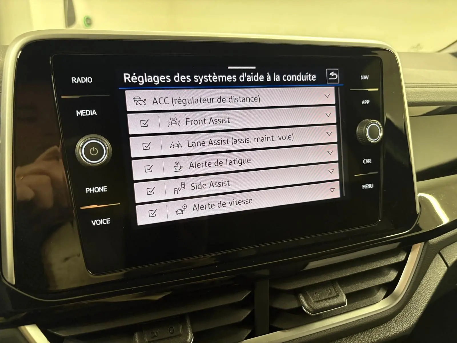 Écran tactile central du Volkswagen T-Roc 2025 affichant les réglages des aides à la conduite, vue rapprochée intérieure.