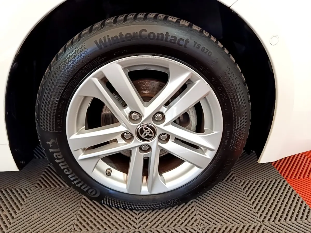 Gros plan sur la roue avant droite d'une Toyota Corolla hybride blanche, avec jante alliage et pneu hiver Continental.