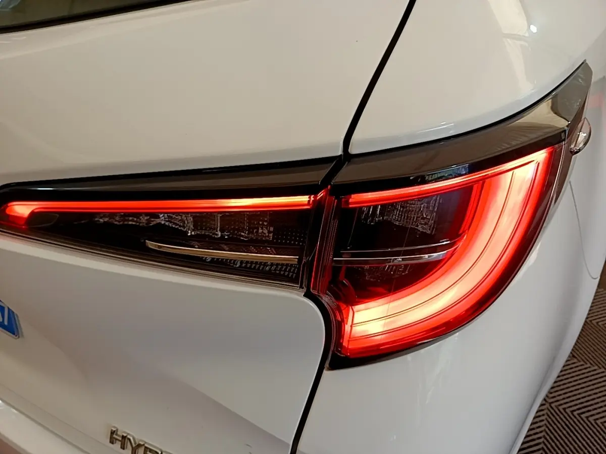 Gros plan sur le feu arrière droit allumé d'une Toyota Corolla hybride blanche de 2022, avec ligne lumineuse LED distinctive.
