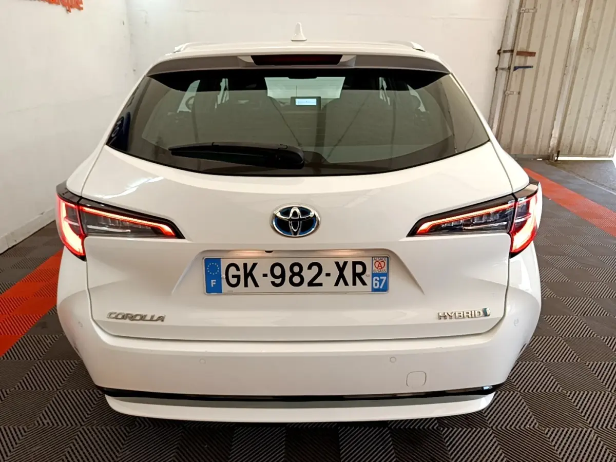 Vue arrière d'une Toyota Corolla hybride blanche 2022 avec feux LED allumés dans un garage.