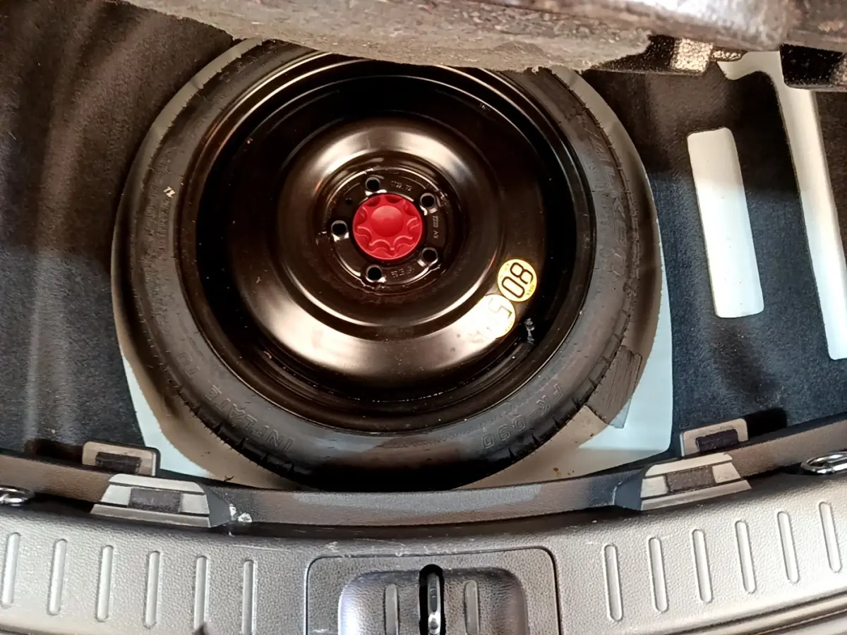 Vue rapprochée de la roue de secours noire avec bouchon rouge dans le coffre d’une Toyota Corolla blanche hybride 2022.