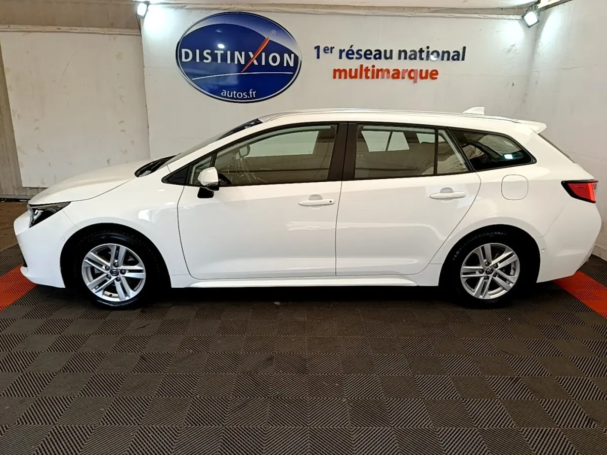 Vue latérale gauche d'une Toyota Corolla blanche hybride 2022 en break, avec rails de toit chromés visibles.