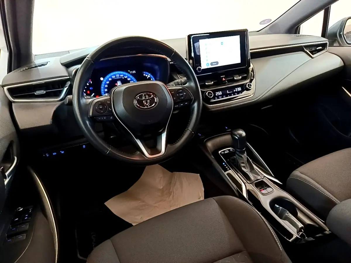 Intérieur de la Toyota Corolla hybride 2022 vu côté conducteur, volant cuir et écran tactile central lumineux.