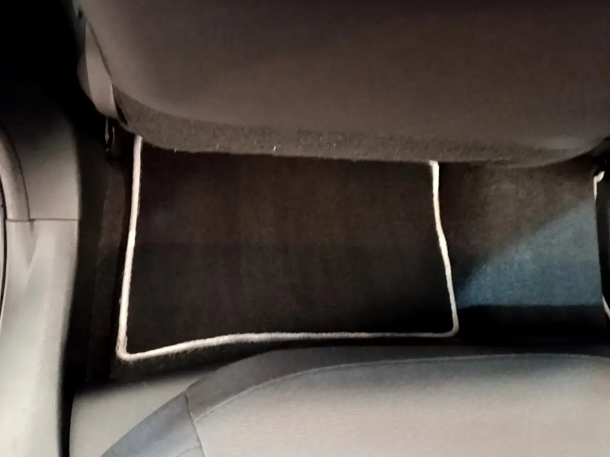 Vue plongeante sur le tapis de sol noir avec bordure claire à l'arrière d'une Toyota Corolla hybride blanche.