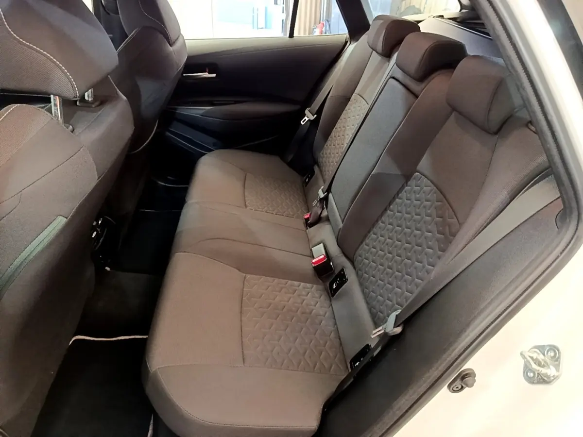 Vue intérieure côté droit sur la banquette arrière grise de la Toyota Corolla hybride blanche 2022 avec portes ouvertes.