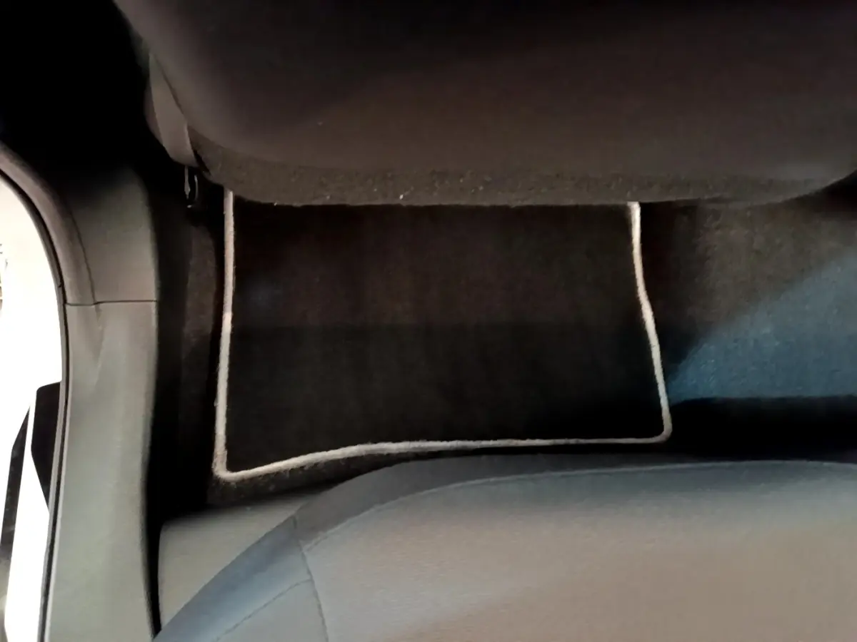 Vue plongeante sur le tapis de sol noir avec bordure claire et partie inférieure du siège avant d’une Toyota Corolla hybride blanche.