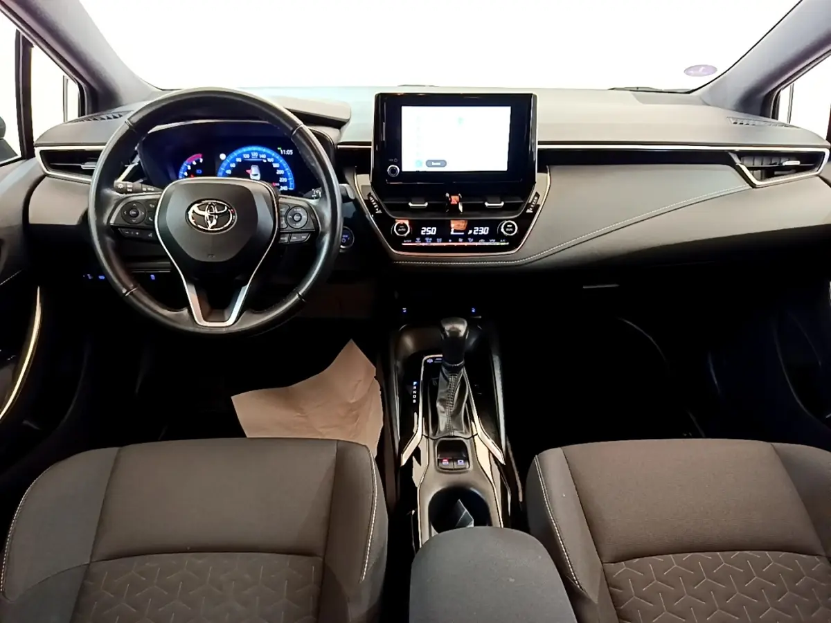 Vue intérieure avant de la Toyota Corolla Hybride 2022, tableau de bord noir avec écran tactile central et volant cuir multifonctions.