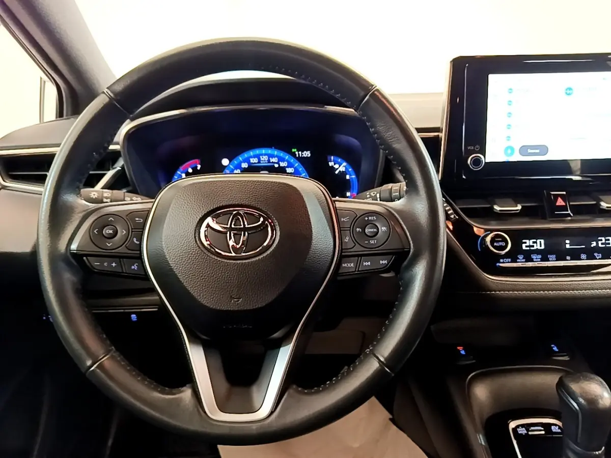 Vue intérieure centrée sur le volant cuir noir et le tableau de bord digital de la Toyota Corolla hybride 2022.