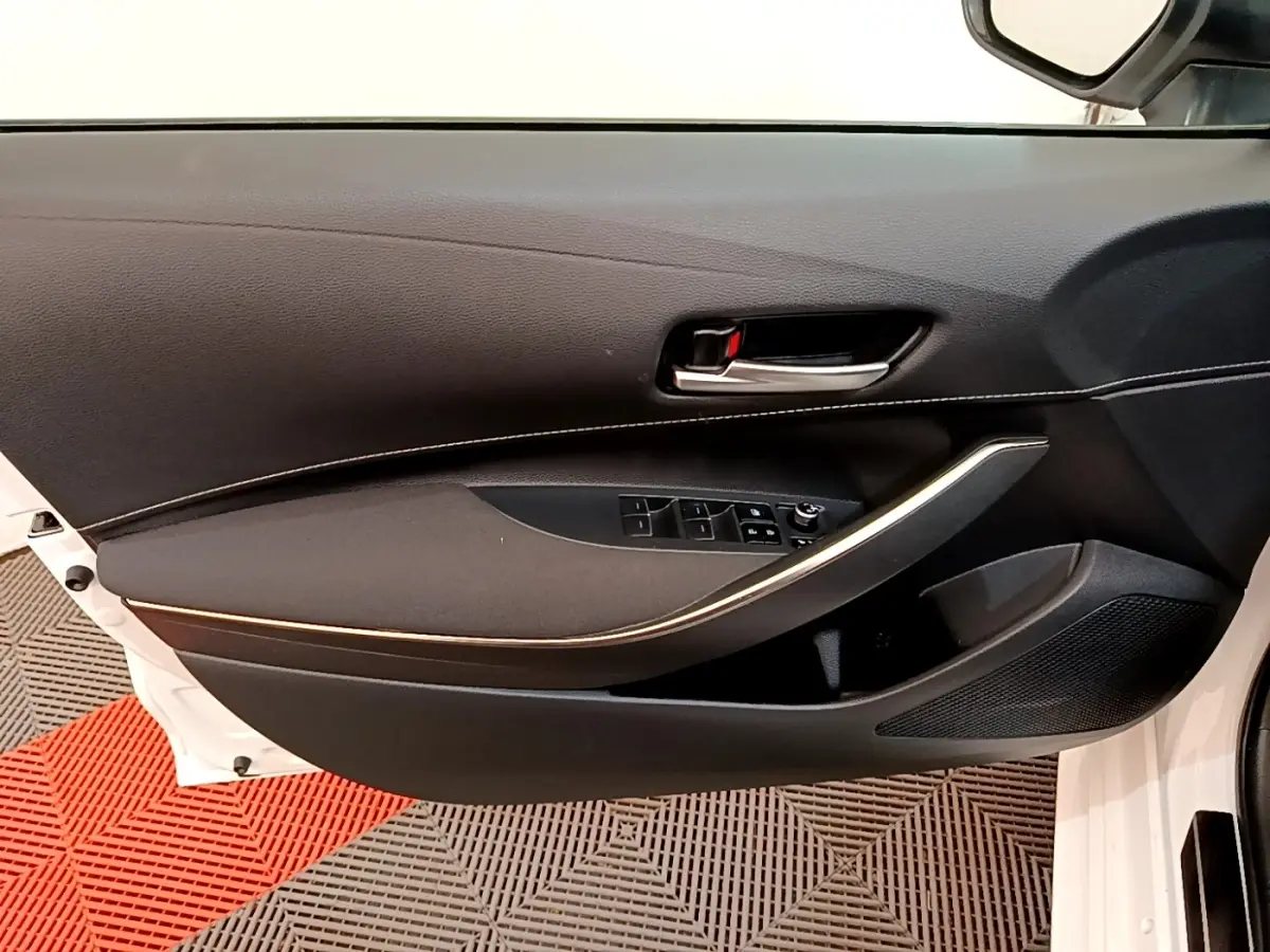 Vue intérieure côté gauche de la porte avant blanche d'une Toyota Corolla hybride avec garniture noire et poignée chromée.