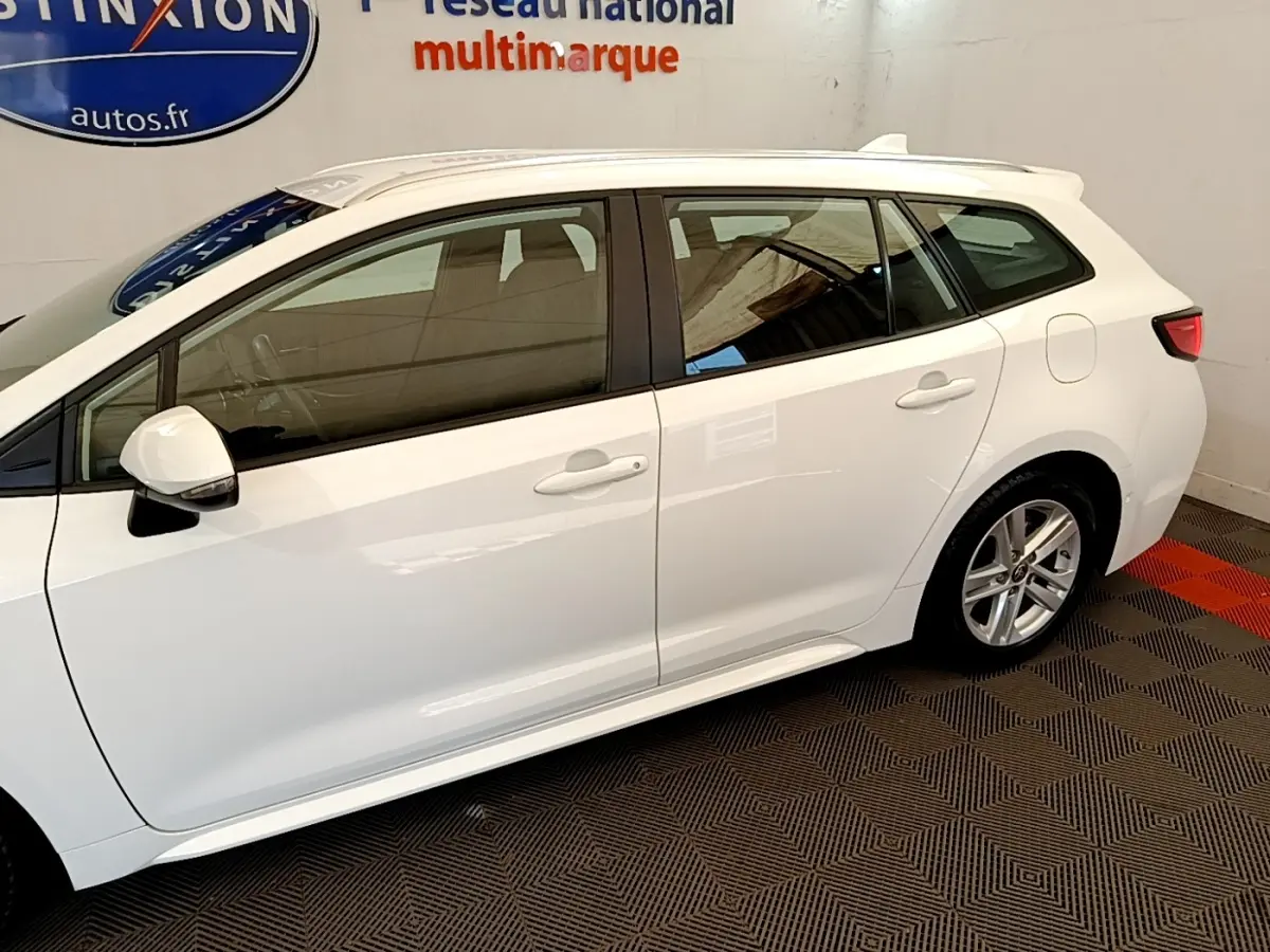 Profil côté gauche de la Toyota Corolla hybride blanche 2022, mettant en valeur les vitres teintées et les jantes alliage.